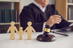 Gavel, sound block and small wooden figurines of husband, wife and kid on judge's table in courthouse during court hearing. Family law, divorce lawyer, joint custody of child and alimony concept