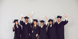 Study abroad website banner. Group of happy smiling diverse academy graduates holding up diplomas. International university students in traditional black academic gowns and caps celebrating graduation