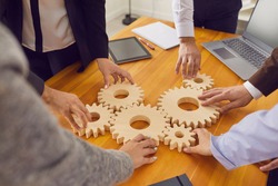Cropped shot of team of company workers joining cogwheels on office table as metaphor for collaboration, teamwork, good business system, finding working solutions and effective management