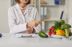 Telehealth and online nutritiologist concept. Woman doctor nutritiologist sitting and pointing at fresh vegan healthy ingredients to patient online during videocall or distant meeting