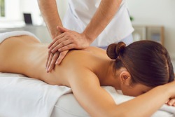 Closeup of relaxed young woman lying face down on massage table and enjoying remedial body massage done by professional masseur in spa salon or wellness center