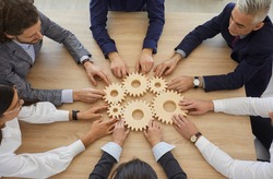 Team of entrepreneurs collaborate and develop effective business system. Group of senior and young business people join gearwheels as metaphor for good cooperation and teamwork, high angle, from above