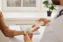 Doctor wrapping young woman's injured hand, close up. Doctor or nurse at modern medical office wrapping patient's sprained wrist with bandage. First aid and professional limb injury treatment concept
