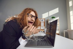 Unhappy tired man stuck at work and can't go home. Desperate employee sitting chained to laptop computer and crying. Office slavery, nine to five job, technology addiction, working extra hours concept