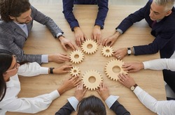 Team of businesspeople developing good business system. Group of senior and young business people sitting around table join gearwheels as metaphor for good effective teamwork. High angle, from above