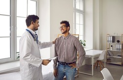 Happy, smiling young man talking to his doctor. Qualified specialist at a modern clinic, hospital or medical center reassuring his male patient after a consultation and health checkup