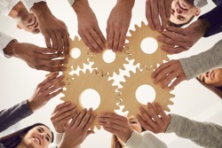 Group of multiracial people joining gear wheels together as metaphor for effective team collaboration, unity, teamwork, finding working solutions and creating business systems. From below, low angle