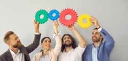 Group of smiling young business people making chain of colorful cogs and gear wheels as symbol and metaphor for creative team and effective teamwork and collaboration. Website header background