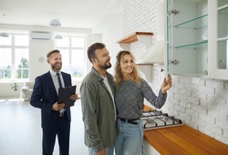 Realtor with customers checking apartmnet. Couple examines furniture in kitchen while inspecting house with real estate agent. Friendly male realtor advises young family before buying new home.