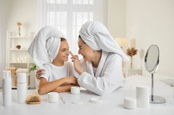 Mother and child having fun during skin care routine. Happy beautiful mommy and pretty little daughter sitting at beauty table, enjoying self care, applying face cream and having good time together