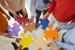 Close up top view of diverse multiracial businesspeople hold jigsaw pieces connect puzzle seek for business solution in office. Employees or colleagues involved in teambuilding activity or training.