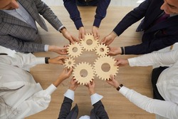 Top view closeup of diverse businesspeople hold connect cog gear engaged in teamwork or teambuilding in office. Employees or colleagues join cogwheels solve business solution or problem together.