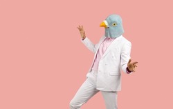 Funny man wearing a pigeon mask dancing and having fun at a crazy fancy dress party. Weird guy ina bird mask dancing isolated on a solid pastel pink colour text copyspace background