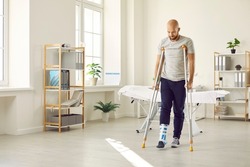 Orthopaedic recovery. Man wearing support adjustable fracture fixator on injured leg walks on crutches in hospital office. Concept of rehabilitation of people after serious physical accident injury.