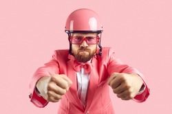 Funny furious tough driver holding pretend steering wheel. Studio shot of man with ginger beard and angry face, wearing pink helmet, funky modern suit, bow tie and sunglasses driving his invisible car