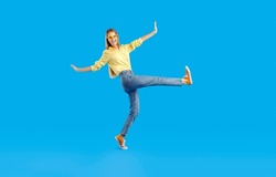Funny cheerful pretty girl in comfortable casual clothes having fun in studio. Happy slim young woman in shirt, jeans, eyeglasses and canvas sneakers walking isolated on solid blue background