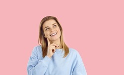 Pensive millennia Caucasian girl isolated on pink studio background think or plan. Thoughtful smiling young woman make decision pondering of good deal or offer. Choice and dilemma concept.