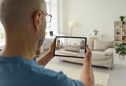 House seller giving a virtual video tour around his recently renovated home. Adult man who plans on selling his sofa or his whole studio apartment takes a photo of the stylish interior on a tablet