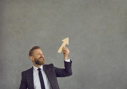 Happy smiling man in suit, businessman or male employee, holding ascending graph chart arrow going up and ahead isolated on grey background. Success, career job skills boost, business growth metaphor