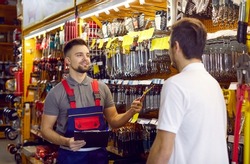 Sales assistant at hardware store helping customer choose tools for home repairs. Salesman with clipboard offering good quality wrench to man who has come to DIY store to buy tools for his garage