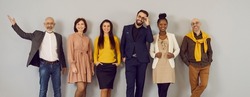 Happy people in clothes suitable for office dress code standing in studio. Mixed race multiethnic group of male and female models in stylish smart casual outfits and glasses posing against grey wall