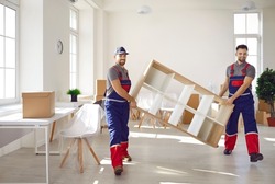 Truck delivery service workers in workwear uniforms removing furniture from house or apartment. Two happy young men from moving company carrying bookshelf together