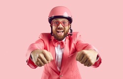 Funny man in pink protective helmet pretends to be motorcycle rider isolated on pink background. Cheerful man in pink formal in suit, glasses and helmet with crazy expression looks at camera. Banner.