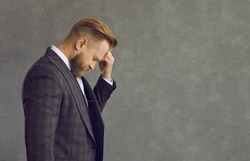 Upset sad depressed businessman in formal suit touching head suffering from headache side view. Studio portrait of people emotion and expression. Frustration and unhealthy anxiety person concept