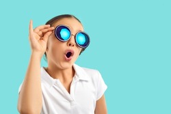 Funny teen child in summer glasses isolated on blue studio background look stunned and amazed. Cool trendy teenager girl in sunglasses shocked by sale deal or seasonal offer. Fashion.