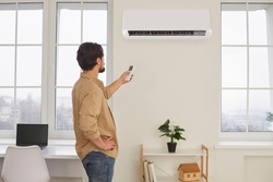 Man with remote control from air conditioner creates comfortable temperature for himself. Young man turns on air conditioner or adjusts mode for air conditioning house. Climate system concept.