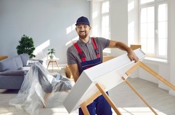 Happy workman carrying furniture. Moving company or truck delivery service worker removing things from old house or apartment. Strong young man in workwear uniform carrying modern table and smiling