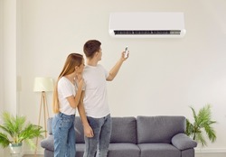 Couple tenants turning on conditioner in living room breathing fresh air. Man and woman renters use condition device at home. Indoors ventilation and modern technology.