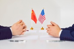 Flags of America and China atand on table during talks between diplomats and businessmen. American and Chinese representatives sit opposite each other to discuss relations between countries.