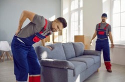 Worker feels sudden pain in his lower back when he tries to lift a heavy sofa. Two young men from a delivery service or a moving company can't carry a heavy couch because one of them gets injured
