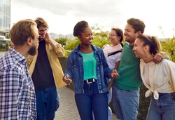 Bunch of joyful diverse college friends meet up in the city. Group of happy beautiful young multi ethnic Caucasian, Afro American and Asian people standing on the street, chit chatting and laughing