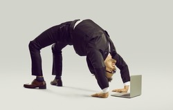 Happy energetic businessman practises yoga positions while working on laptop computer. Funny fit flexible young man in suit and glasses doing bridge pose on studio floor while using modern notebook PC