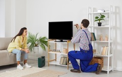 Female customer watch male mechanic or electrician repair TV set at home. Man repairman or engineer fix television set at woman client house. Household services concept.