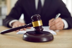 Close-up judge wooden gavel symbolizing legal proceedings or lawsuit from private person or business requiring services of lawyer or juridical company on table in front of blurred man