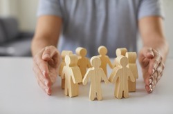 Social protection. Wooden figurines of people surrounded by man's hands symbolizing care for employees, customers or family. Close-up of figurines of people standing in circle on table and male