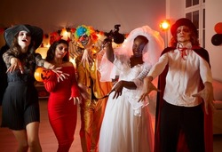 Portrait of various horror room characters in creepy costumes pretending to be walking dead. People dressed as vampire, witch, dead bride, clown and devil walk like zombies in dark room with red