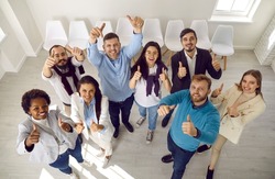 Team of satisfied people who make happy gesture by raising their hands with thumbs up demonstrating success. Top view of multiracial people expressing their support while standing in waiting room.