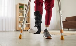 Man with broken leg or foot injury walking with crutches at home. Young guy wearing ankle support brace or fracture fixator with adjustable straps standing in living room. Cropped low section close