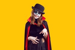Preteen girl with creative Halloween make-up and wearing dracula cape isolated on orange background. Portrait of smiling child having fun at carnival party. Halloween party concept. Web banner.