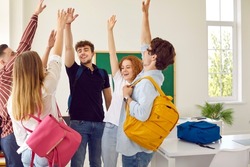 Intelligent High school students rise hands up at modern classroom with green chalkboard on background. Celebration of successfully passed exams, well-done creative work, week end or vacation.