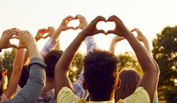 Happy adult diverse multiethnic people raise hands up in air, do heart shaped gestures, share good vibes, hope for peaceful future, send kind wishes to universe. Outdoor outside back view group shot