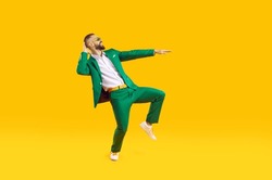 Cool and stylish young man is having fun dancing celebrating Saint Patricks Day. Caucasian man in stylish green suit, white shirt and sunglasses smiling while dancing on orange background. Web banner