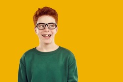 Portrait happy smiling red-haired confident boy in transparent glasses with a funny expression looks away, dressed in a green sweater. Isolated studio photo on a bright yellow background.