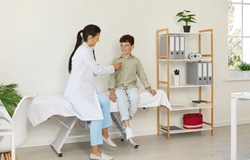 Child getting health checkup in exam room at doctor's office. Pediatrician sitting on medical couch together with school boy and examining his heart or lungs with stethoscope. Hospital visit concept