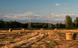 High voltage power line near the bales of straw on a mown wheat field after harvesting.