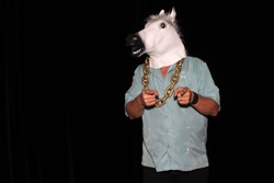 An unidentifiable man wears a White Rubber Horse Head Mask while wearing a Gold Chain and points to the camera in a Photo Booth. With Black velvet curtains and room for your text